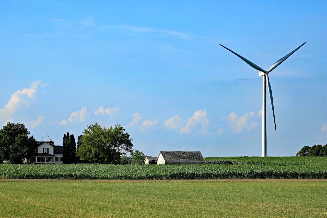 A scenic view of a wind turbine in a rural farm setting under a clear blue sky.